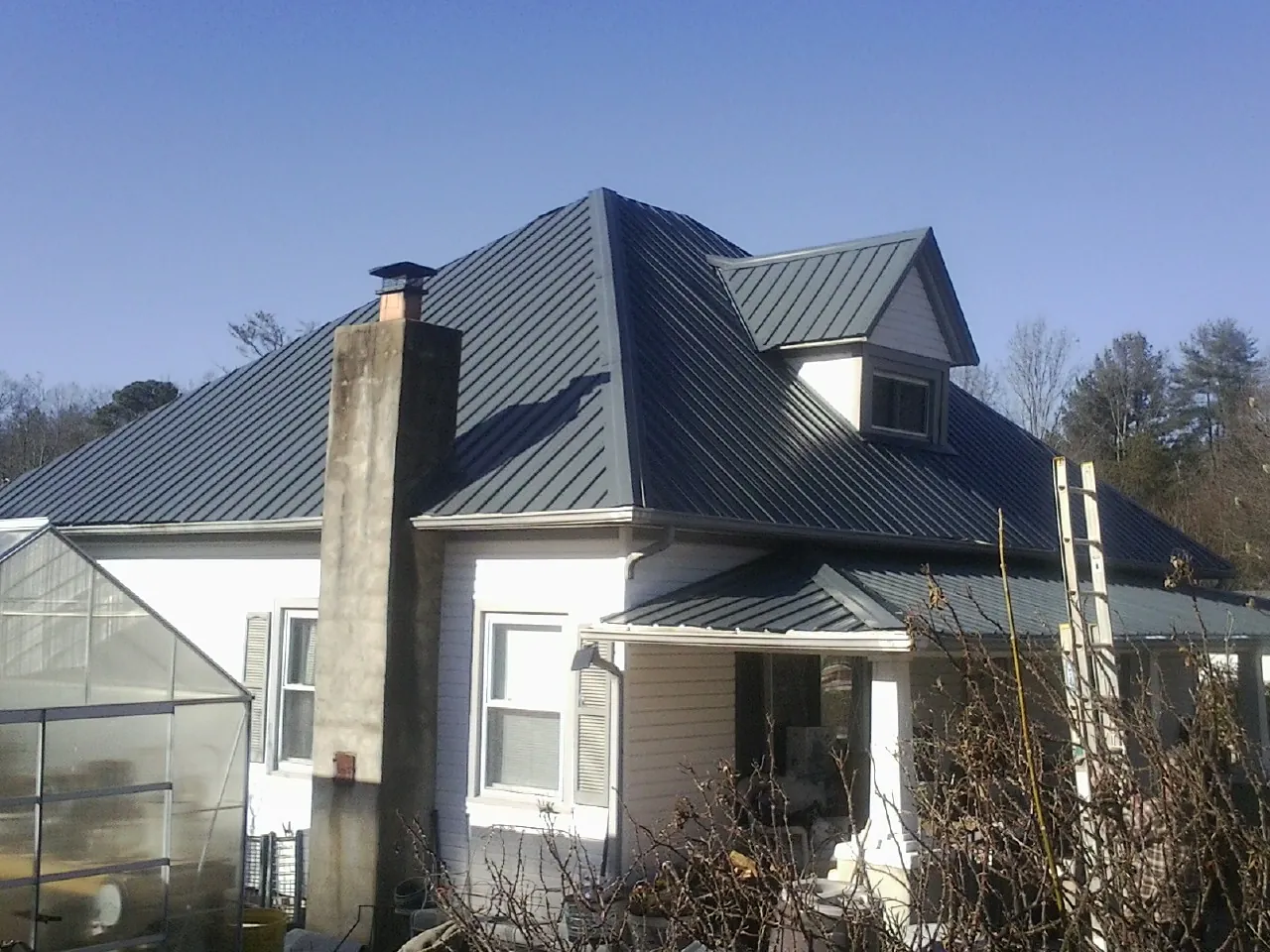 Dark blue standing seam metal roof on a white farmhouse with dormer — Slate & Tile Roof Repair by Roofing Brothers in Bay City