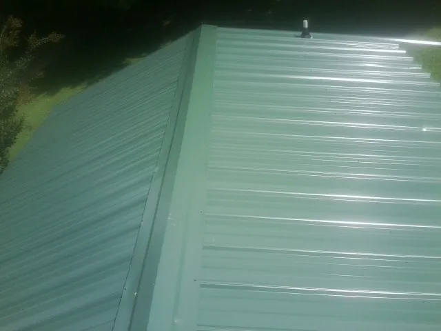 New green metal panels meeting at the ridge of a roof — Flat Roof Repair work by our crew in Bay City