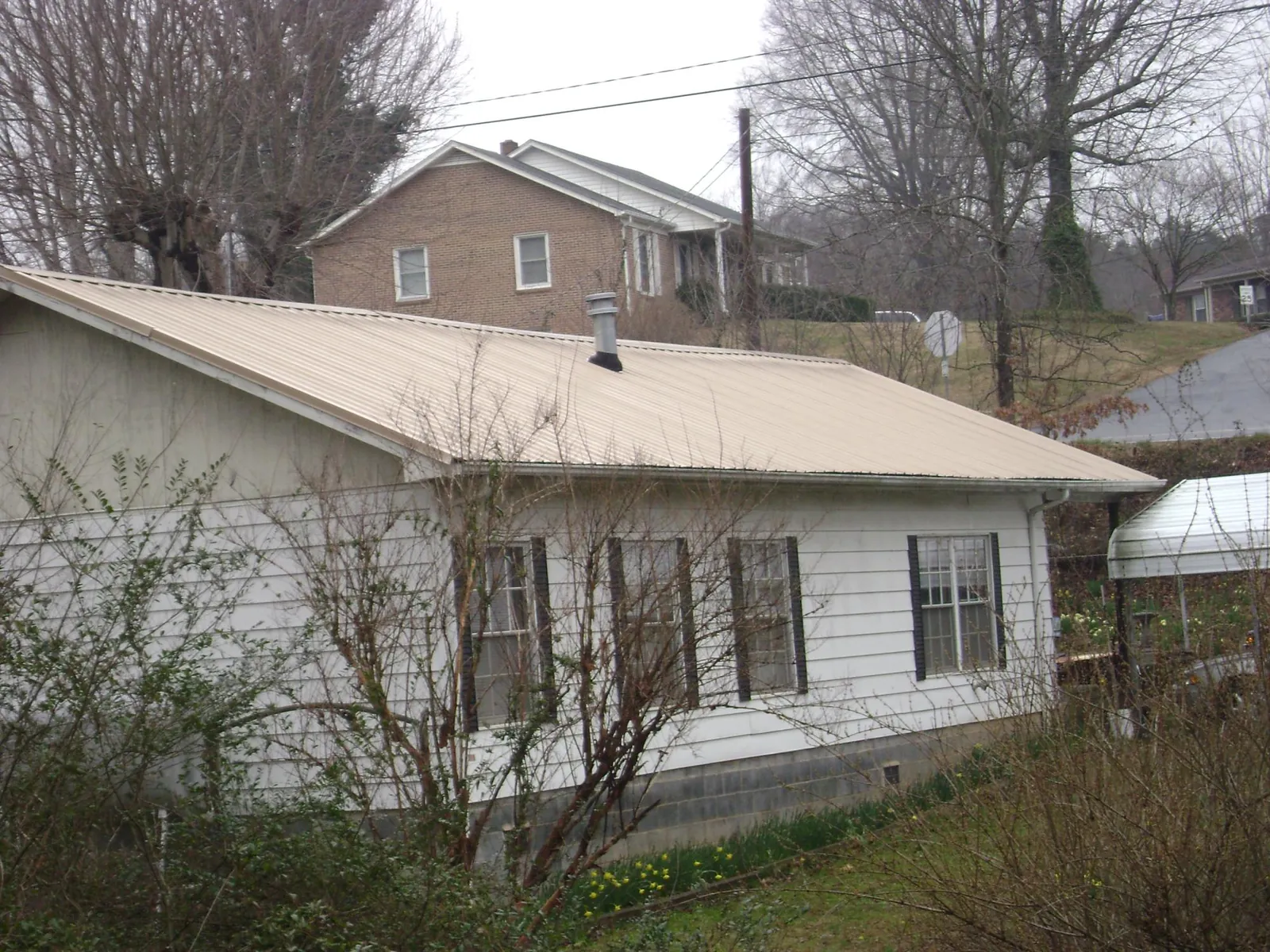 Tan metal roof on a white sided house set into a hillside — Commercial Roofing by Roofing Brothers in Bay City